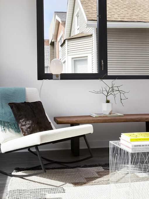 A white chair with a blue pillow is in front of a window.