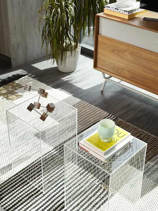 A white and black striped rug with a glass table and a white vase with a plant on it.