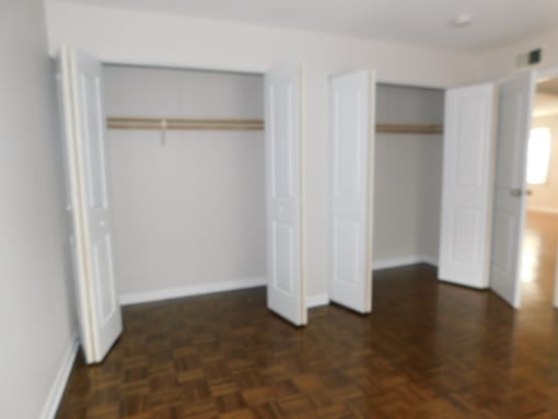 A room with a wooden floor and white walls with open doors.