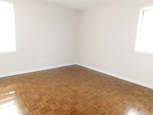 A room with wooden flooring and two windows.