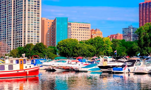 A red boat is docked in a marina with other boats and buildings in the background.