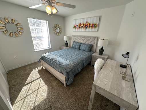 A bedroom with a bed, desk, and a ceiling fan.