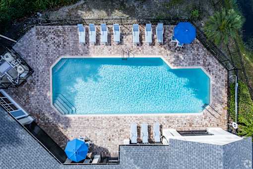 A rectangular pool surrounded by a brick patio and lounge chairs.