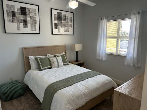 A bedroom with a bed, nightstand, and two framed artworks on the wall.