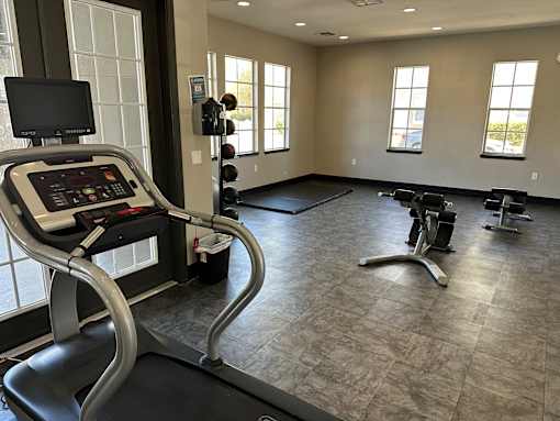 A treadmill with a monitor and control panel is in a spacious gym with other exercise equipment.