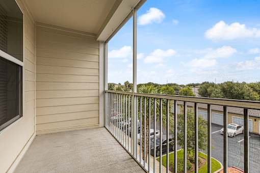 A balcony with a view of a parking lot and trees.