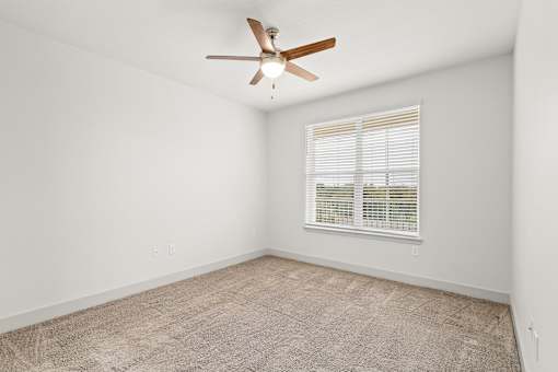 A room with a ceiling fan and a window with blinds.