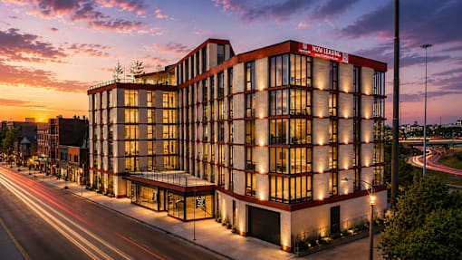 A modern building with a red and white facade is illuminated at dusk.