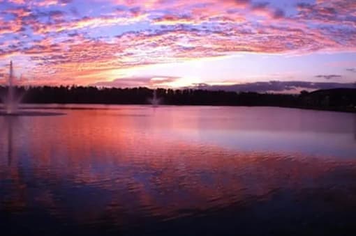A beautiful sunset over a lake with a fountain in the foreground.
