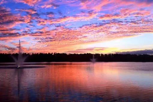 A fountain in the middle of a lake with a beautiful sunset in the background.
