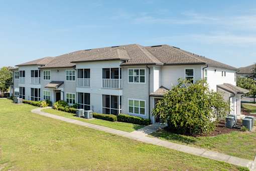 A large white building with a brown roof and a green lawn in front.