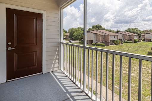 A brown door is on the left of a balcony with a metal railing.