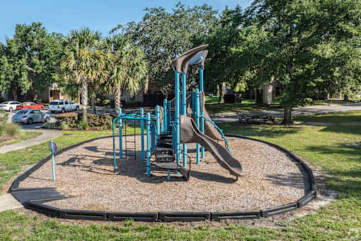 A playground with a blue slide and a brown sandbox.