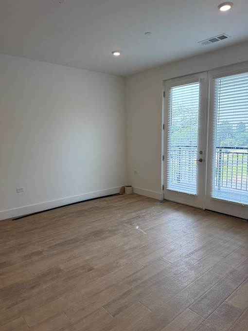A room with a sliding glass door and wooden flooring.