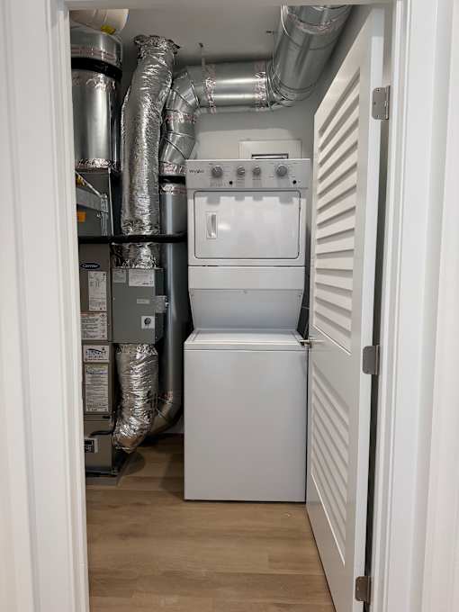 A white washing machine is in a small room with a wall of pipes.