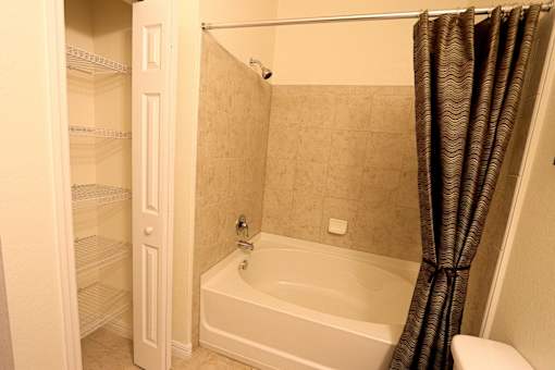 A white bathroom with a tub, shower, and open door to a pantry.