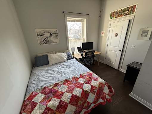 A bedroom with a bed, desk, chair, and window.