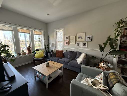 A living room with a grey couch, a wooden coffee table, and a large window.
