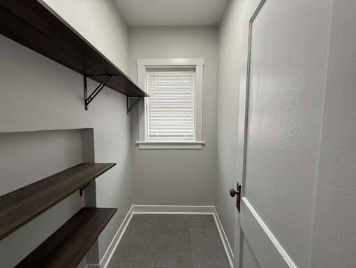 A hallway with a door on the right and a window with blinds on the left.