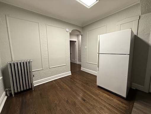 A white refrigerator sits in a room with wooden floors and white walls.