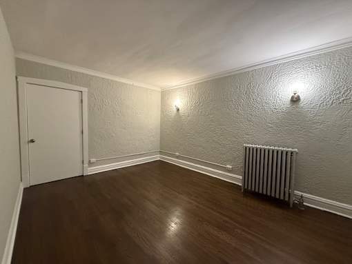 A room with a white door, a radiator on the wall, and a wooden floor.