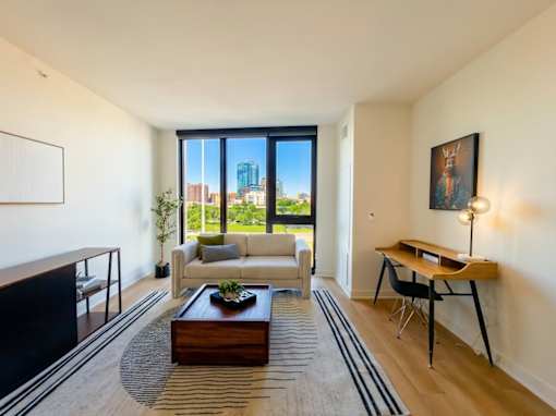 A living room with a white couch, a coffee table, and a large window overlooking the city.