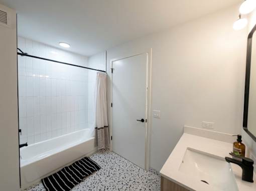 A bathroom with a white sink, a white bathtub, and a black and white floor mat.
