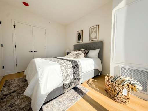 A bedroom with a bed, two pictures on the wall, and a basket on the floor.