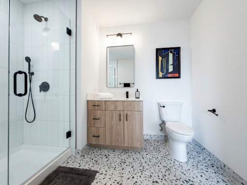 A bathroom with a white toilet, a wooden cabinet, and a shower with a black shower head.