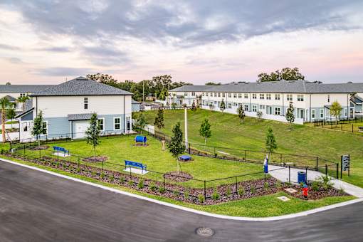 A large white building with a blue door is surrounded by a grassy area and a fence.