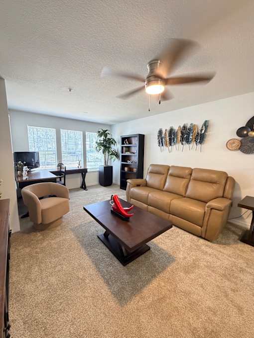 A ceiling fan is on in a room with a brown carpet.
