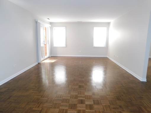 A room with wooden flooring and two windows.