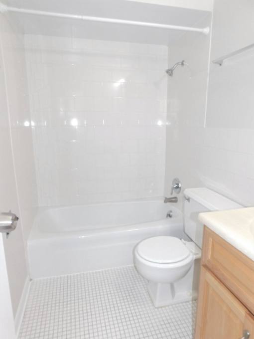 A white toilet sits in a bathroom next to a bathtub.