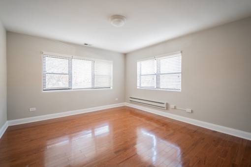 A room with wooden floors and two windows with blinds.