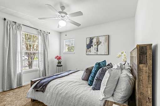 A bedroom with a bed, pillows, a ceiling fan, and a window with curtains.