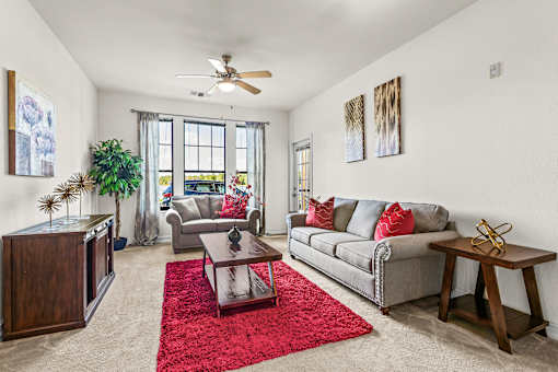 A living room with a grey couch, a red rug, and a ceiling fan.