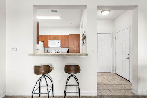 A kitchen with white walls and a counter with two stools.