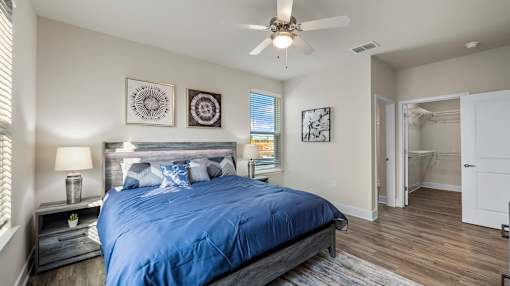 A bedroom with a blue bedspread and a ceiling fan.