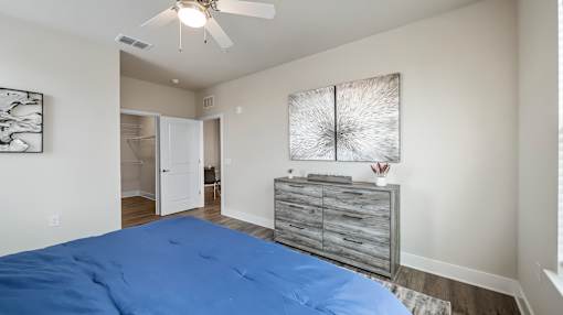 A bedroom with a blue bedspread and a ceiling fan.