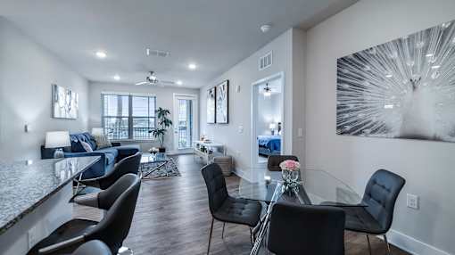 A modern living room with a glass dining table and black chairs.