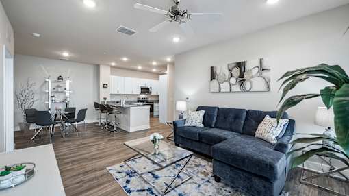 A modern living room with a grey sofa and a dining area in the background.