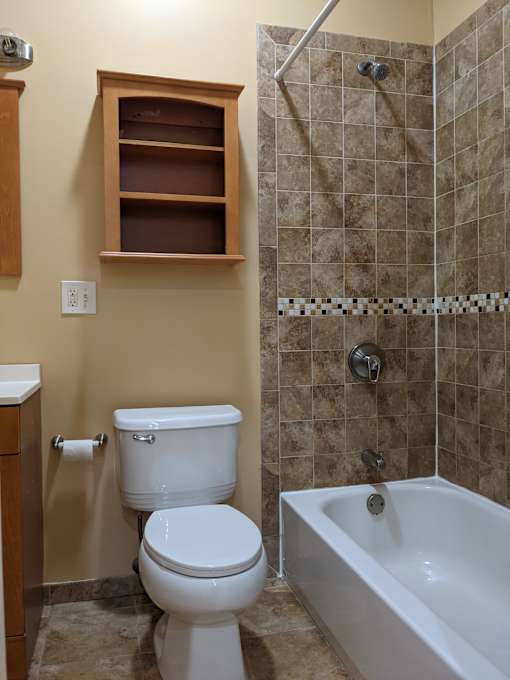 A white toilet sits next to a white bathtub in a tiled bathroom.