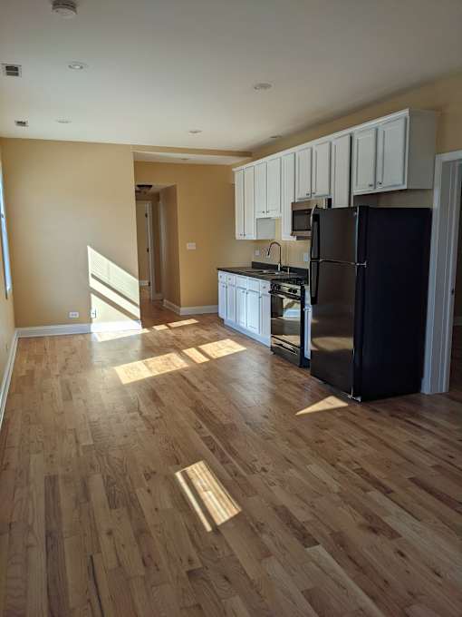 A kitchen with wooden floors and a black refrigerator.