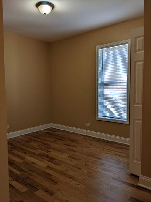 A room with wooden flooring and a window with blinds.