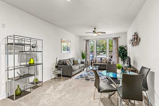 A living room with a grey couch, a glass table, and a glass shelf with vases.