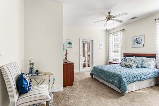 A bedroom with a bed, chair, and ceiling fan.