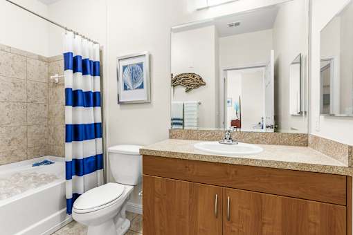 A bathroom with a white toilet, a white sink, a blue and white striped shower curtain, and a wooden cabinet.