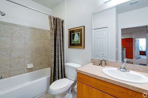 A bathroom with a white toilet, a white sink, a white bathtub, and a brown picture frame.