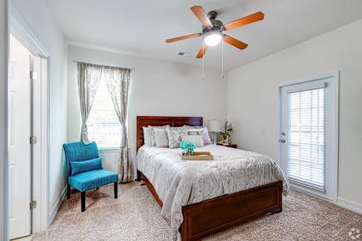 A bedroom with a bed, chair, and ceiling fan.