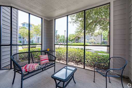 A patio with a black metal bench and a glass table.